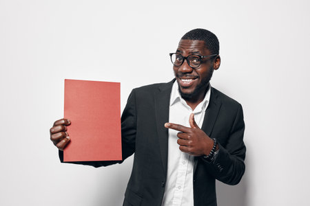 African American man with dark skin wearing glasses and suit holding red paper and smiling while...