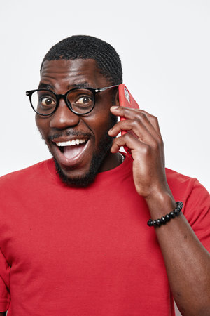 African man with dark skin wearing glasses and red sweater talking on smartphone with excited...
