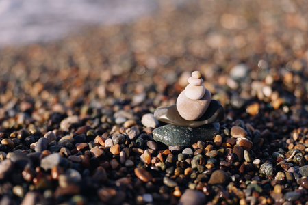 Close view of a tiny stack of smooth stones on a pebbled beach with calm water in the background,...