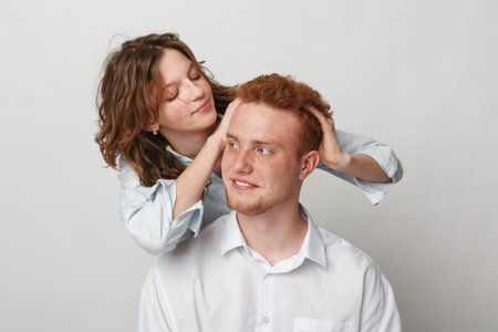 Young woman gently massages young manâ€™s head and hair in white studio. Concept of care,...