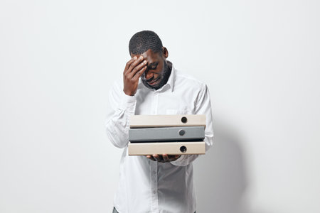 African man with dark skin holding folders and touching forehead in stress or headache. Businessman...