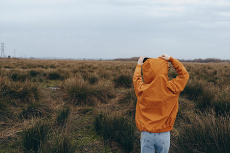 Woman lifestyle concept with a person wearing an orange jacket standing in a grassy field under...