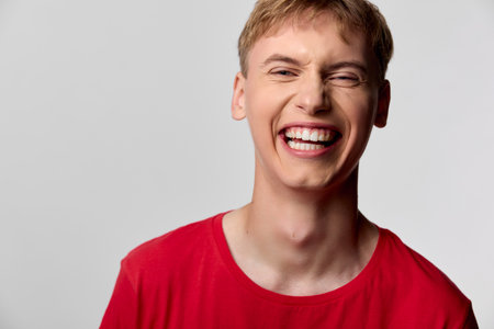 Smiling man in a red shirt grins with bright happiness and joyful energy, a candid studio closeup...