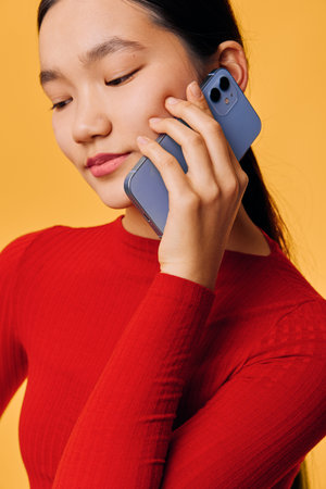 Young woman in red shirt holding smartphone to ear speaking and listening on call with calm...
