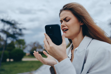 upset woman holding smartphone with frustrated expression outdoors during cloudy weather upset woman...