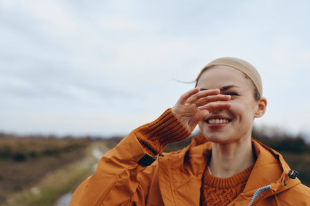 Smiling woman lifestyle outdoors in autumn wearing orange jacket and sweater covers face with hand....