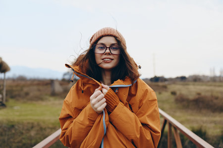 Young woman lifestyle in orange jacket and hat enjoys autumn outdoors holding a dry leaf. Casual...