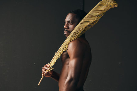 African man with dark skin holding large golden feather in creative conceptual visual style....