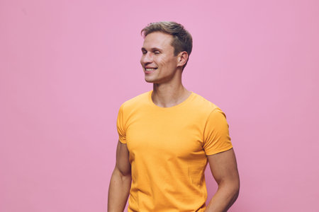 Smiling young man wearing bright yellow t-shirt looking away on pink background studio portrait...