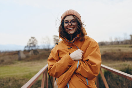 Smiling woman in orange jacket and brown hat enjoys autumn outdoors on a bridge. Lifestyle concept...