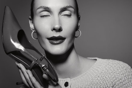 Closeup of white woman with pale skin holding shiny high heel shoe near face, eyes closed, wearing...