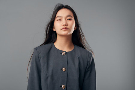 Young woman with long dark hair wearing a gray jacket posing confidently in studio. Portrait of...
