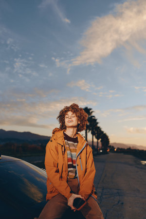 Woman smile outdoors wearing rainbow sweater and orange jacket, holding smartphone, relaxed...