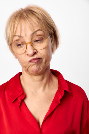 Blonde middle aged woman in glasses and red blouse looks confused and skeptical with pursed lips on...