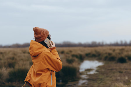 Woman lifestyle concept with a young woman in an orange jacket and brown hat talking on the phone...
