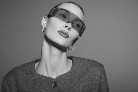 Stylish white woman with pale skin wearing futuristic sunglasses and textured jacket looks confident...