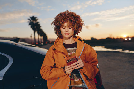 Young woman with curly hair wearing a rainbow sweater and orange jacket smiling while using...