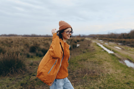 Young woman lifestyle in casual autumn clothes walking on rural path. She wears orange jacket and...