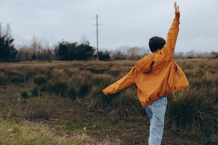 Young woman lifestyle concept with a person wearing an orange jacket outdoors in a natural field....