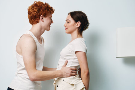 Young couple, man and woman standing close, looking at each other with soft expressions in casual...