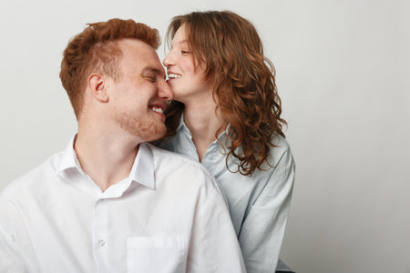 Happy young couple in white shirts share intimate moment, smiling and close together against plain...