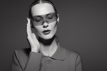 Young white woman with pale skin wearing futuristic translucent glasses and vintage style coat poses...
