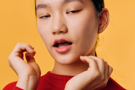 Young woman with closed eyes and open mouth posing with hands near face wearing red top on orange...