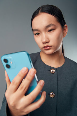 Young woman with dark hair wearing black coat looking at smartphone screen with focus and slight...