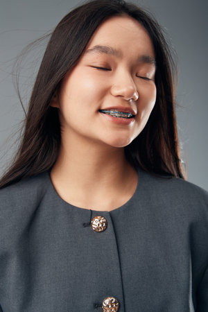 Young woman smiling with closed eyes wearing braces on teeth and long dark hair. Portrait with...