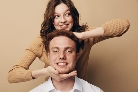 Smiling young woman with brown hair playfully framing the face of a happy redhead man in white...