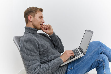 young caucasian man using laptop sit floor wearing grey turtleneck sweater blue jeans technology...