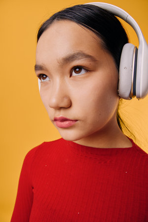 Young woman wearing wireless headphones in red sweater looking sideways with focused expression on...