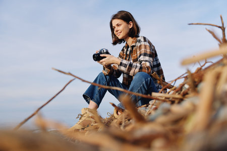 Woman photographer crouches on driftwood by the shore, holding a camera and scanning the scene for...
