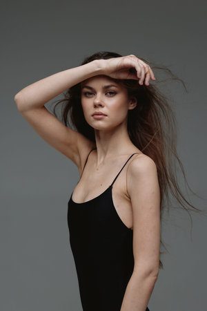 Portrait of a young woman with long hair wearing a black dress posing with hand on forehead against...