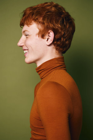 Young man with red hair and freckles wearing brown turtleneck sweater in profile smiling cheerfully...