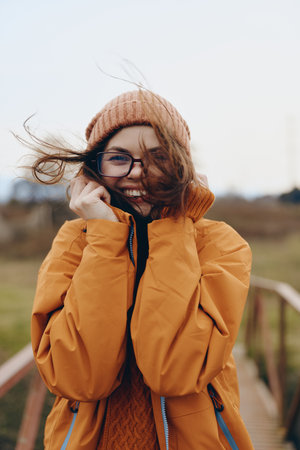 Smiling woman lifestyle outdoors in warm orange jacket and knit hat embraces cold weather with joy....