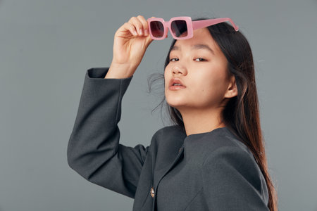 Woman with long hair wearing black jacket holding pink sunglasses near face posing with confident...