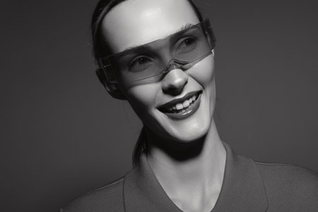 Smiling young white woman with pale skin wearing transparent glasses looks right, showing teeth....