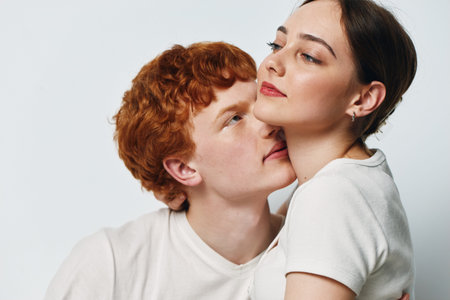 Couple, young man and woman embracing while sitting close together with affectionate expression on white background in studio. Intimate moment of love and connection between two people.の写真素材