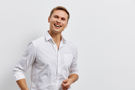 Smiling young man with bright cheerful expression wearing white shirt on plain white background. Studio portrait of happy male, casual style, positive mood, clean look, adult fashion, lifestyle concept.の写真素材