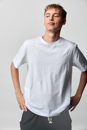 Casual male model in a plain white t shirt stands in a studio, confident pose with hands on hips,...