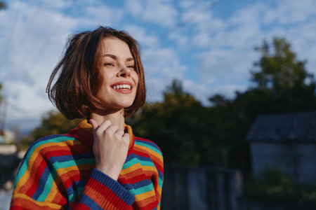 Young woman mid-20s smiling woman in a colorful striped sweater and casual outfit, outdoor portrait...