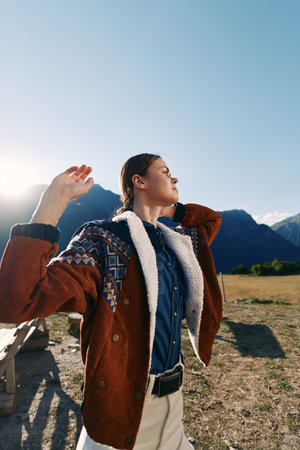 Woman portrait in mountains outdoors wearing a warm patterned jacket, basking in golden sunlight in...