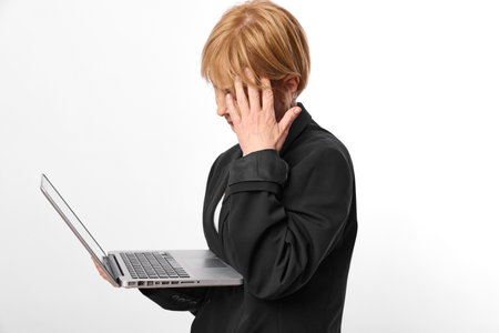 Redhead woman in black jacket holds open laptop and looks at screen with concern or confusion...