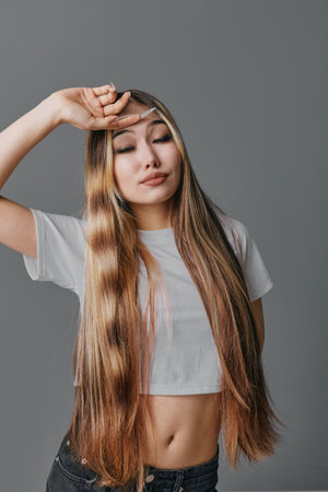 Woman with long straight hair in casual white cropped t shirt posing with eyes closed and hand on...