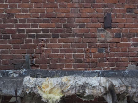 Suburban landscape. Old, textured brickwork made of multicolored bricks and a heating pipeの写真素材