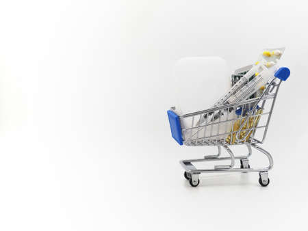 The second, the third wave of coronavirus. Mini shopping cart with medicine from Covid-19. Vaccine, syringes and pills on a light background.の写真素材