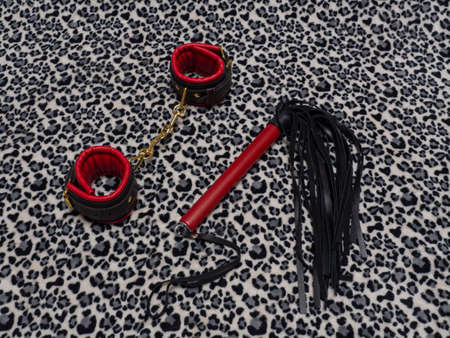 Toys for adults. Red and black leather handcuffs and a whip on a leopard background. BDSM equipment.の写真素材