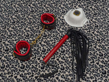 Toys for adults. Medical, aerosol mask leather red and black handcuffs and a whip on a leopard background. BDSM equipment.の写真素材