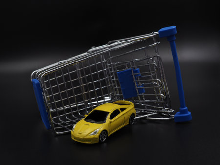 Buying or renting a car. Car sharing. Yellow toy car in a shopping cart on a black gradient background. Collapse of prices, discount on the car.の写真素材